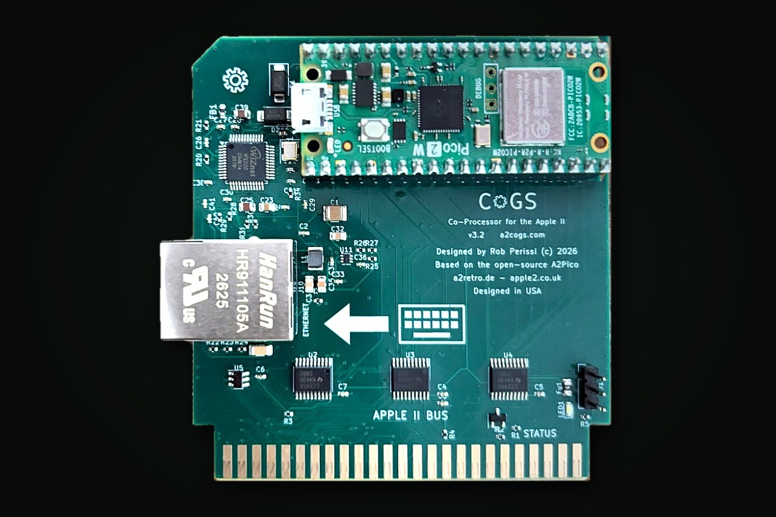 The CoGS v3.2 production card, photographed: green PCB with gold edge connector, a Raspberry Pi Pico 2 W across the top, W5500 Ethernet with a silver RJ45 jack at the rear, three bus transceivers over the Apple II bus, and a status LED. Designed by Rob Perissi, based on the open-source A2Pico carrier by Glenn Jones, Oliver Schmidt, and Ralle Palaveev.